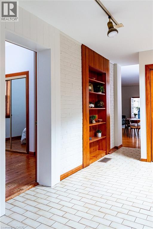 Hallway featuring rail lighting, brick wall, built in shelves, and brick patterned floors - 218 Bay Street S, Hamilton, ON
