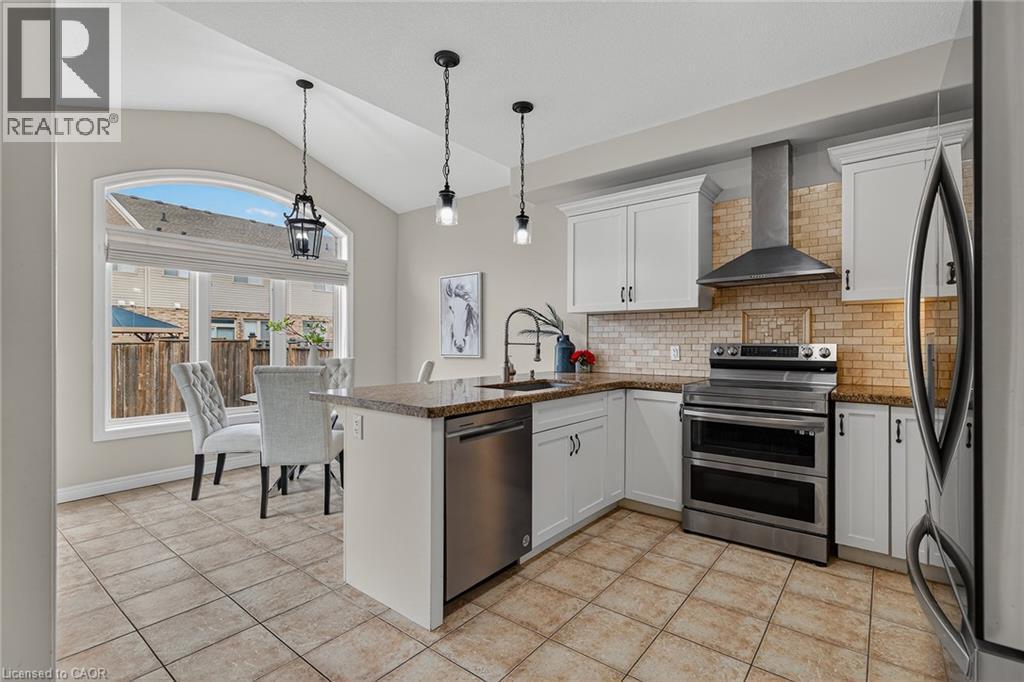 Kitchen featuring stainless steel appliances, a peninsula, lofted ceiling, dark stone counters, and white cabinetry - 100 Garinger Crescent, Binbrook, ON - Indoor Photo Showing Kitchen With Stainless Steel Kitchen With Upgraded Kitchen