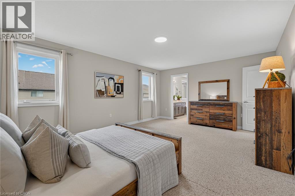Carpeted bedroom featuring multiple windows and connected bathroom - 100 Garinger Crescent, Binbrook, ON - Indoor Photo Showing Bedroom