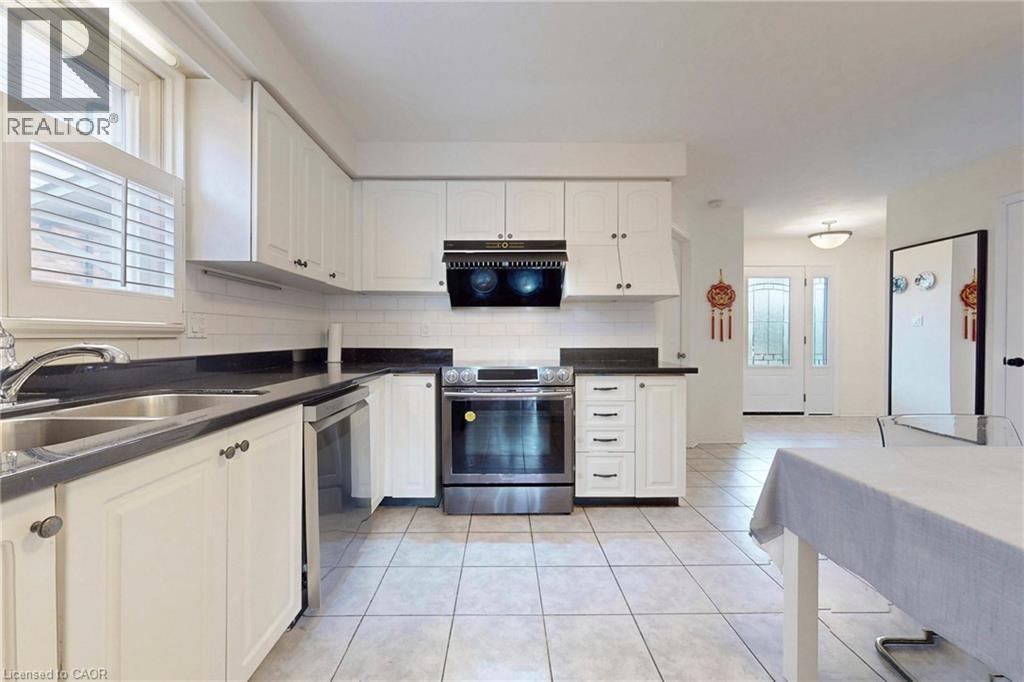 Kitchen featuring stainless steel appliances, white cabinets, dark countertops, and light tile patterned flooring - 62 Como Place, Hamilton, ON - Indoor Photo Showing Kitchen With Double Sink