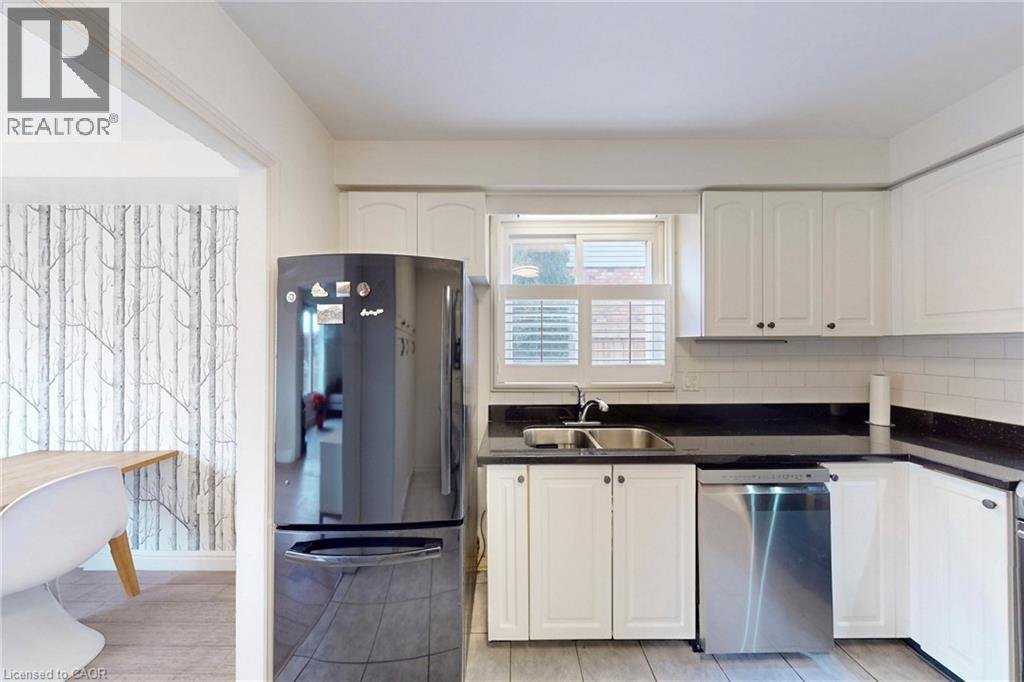 Kitchen featuring freestanding refrigerator, stainless steel dishwasher, white cabinets, decorative backsplash, and dark stone counters - 62 Como Place, Hamilton, ON - Indoor Photo Showing Kitchen With Double Sink