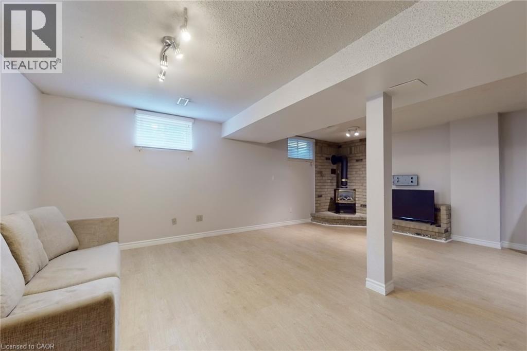 Basement with a wood stove, light wood-style flooring, plenty of natural light, and a textured ceiling - 62 Como Place, Hamilton, ON - Indoor Photo Showing Basement