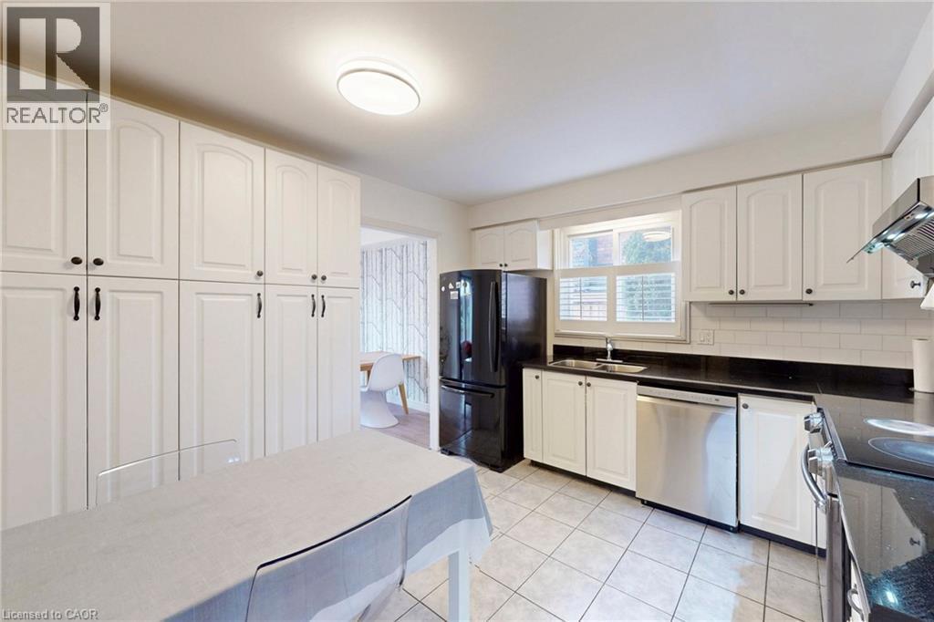 Kitchen featuring stainless steel appliances, white cabinetry, backsplash, light tile patterned floors, and dark stone countertops - 62 Como Place, Hamilton, ON - Indoor Photo Showing Kitchen