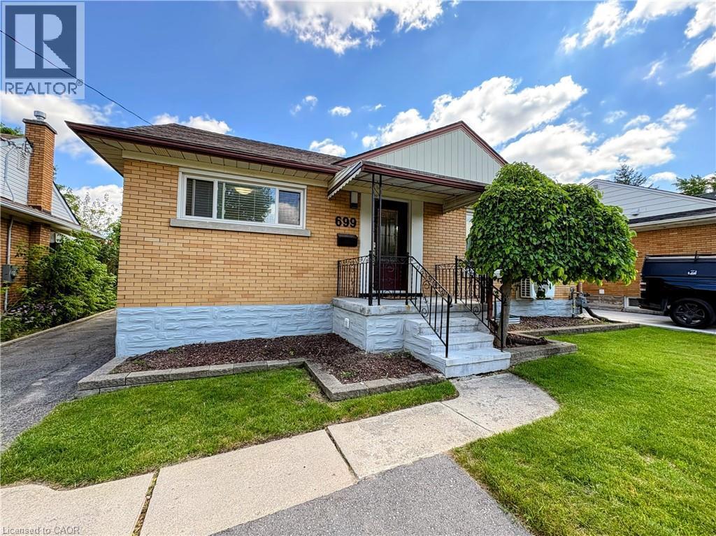 Brick exterior featuring a covered entry, concrete steps with metal railings, a paved driveway, and a front yard with grass and mature landscaping - 699 Frederick Street, Kitchener, ON