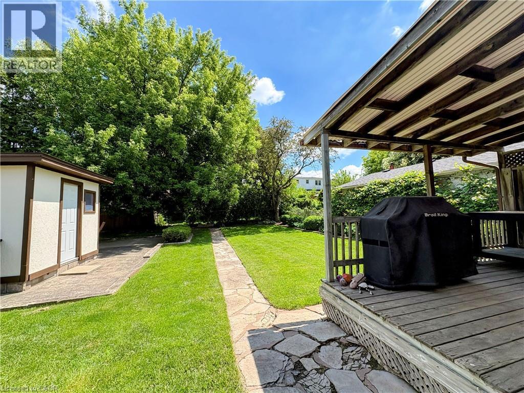Spacious backyard featuring a covered wood deck, expansive lawn, stone pathway, and a detached storage shed with stucco siding - 699 Frederick Street, Kitchener, ON