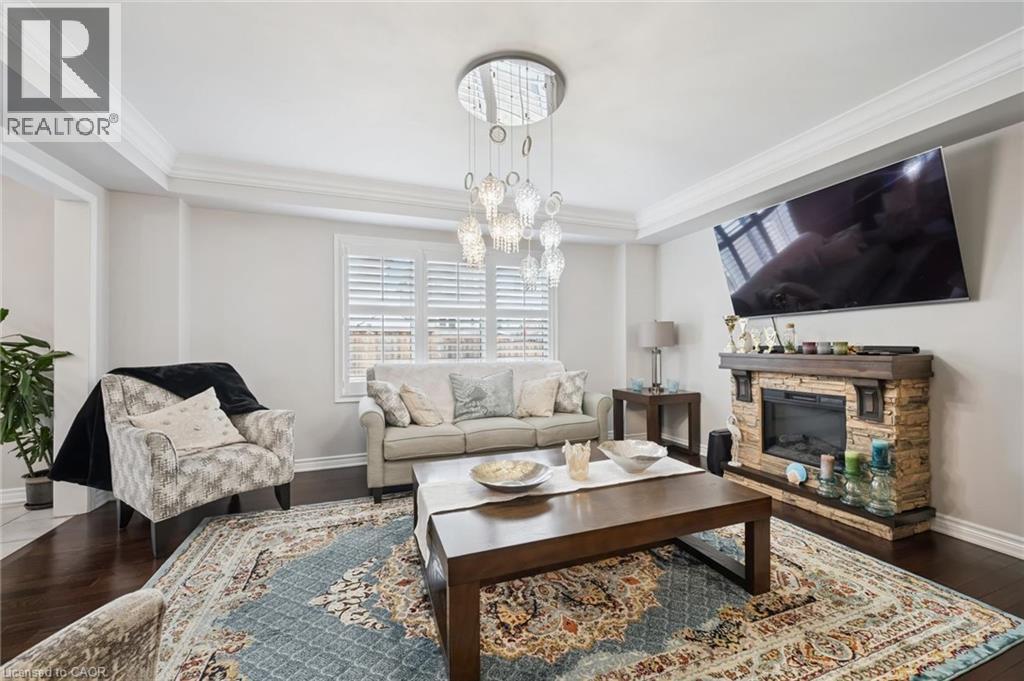 Living area featuring hardwood / wood-style flooring, suspended lighting, a fireplace, ornamental molding, and a raised ceiling - 38 Park Glen Street, Kitchener, ON - Indoor Photo Showing Living Room With Fireplace