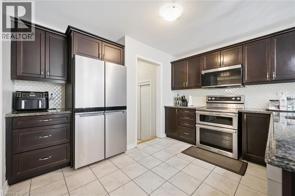 Kitchen with dark wood finish cabinetry, dark stone counters, stainless steel appliances, tasteful backsplash, and light tile patterned flooring - 38 Park Glen Street, Kitchener, ON - Indoor Photo Showing Kitchen With Stainless Steel Kitchen