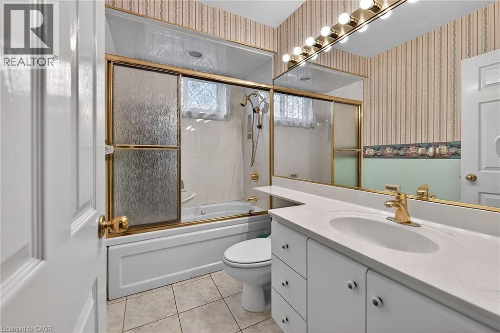 Bathroom with vanity, light tile patterned floors, bath / shower combo with glass door, and wallpapered walls - 21 Bluebird Avenue, Hamilton, ON - Indoor Photo Showing Bathroom