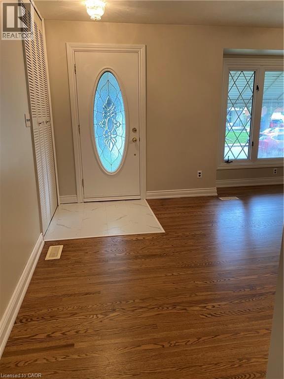 Entryway featuring a white door with decorative oval glass, white tile flooring, and warm wood-finish flooring extending into the room - 21 Bluebird Avenue, Hamilton, ON