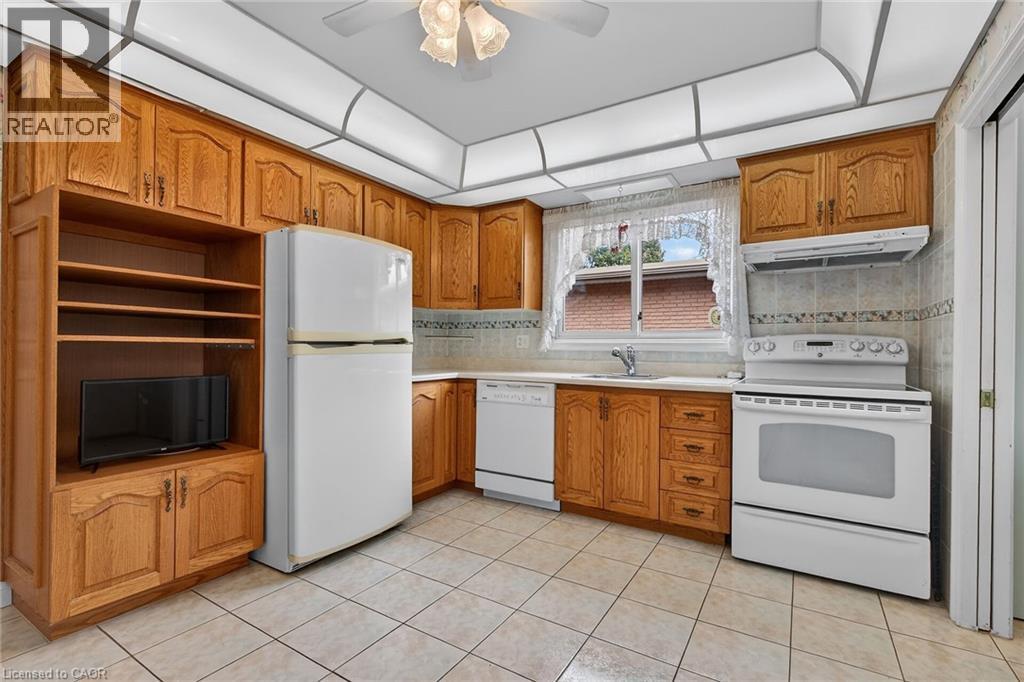 Kitchen featuring white appliances, wood finish cabinetry, ceiling fan, light countertops, and light tile patterned flooring - 21 Bluebird Avenue, Hamilton, ON