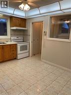 Kitchen featuring wood cabinetry, white appliances, tile flooring, and a drop ceiling with integrated lighting -