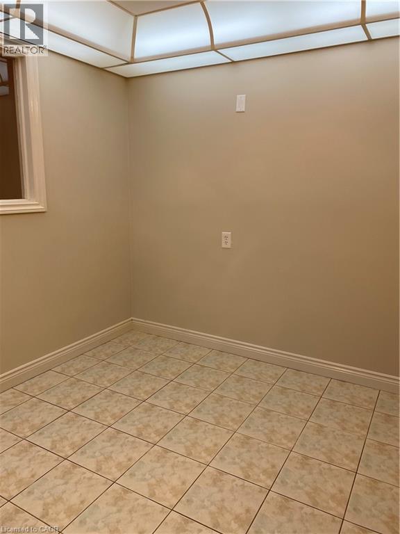 Room featuring neutral-toned walls, square tile flooring, a window with white trim, and a ceiling-mounted light fixture - 21 Bluebird Avenue, Hamilton, ON