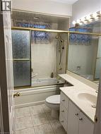 Full bathroom featuring a tub/shower combination with a gold-toned framed enclosure, a single vanity with storage cabinetry, and tiled flooring -