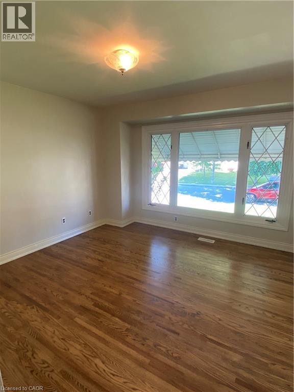 Hardwood flooring throughout this room featuring a large window with decorative mullions and white trim - 21 Bluebird Avenue, Hamilton, ON