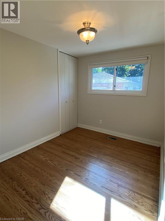 Light-filled room featuring hardwood flooring, a white-framed window, and a built-in closet with bifold doors - 21 Bluebird Avenue, Hamilton, ON