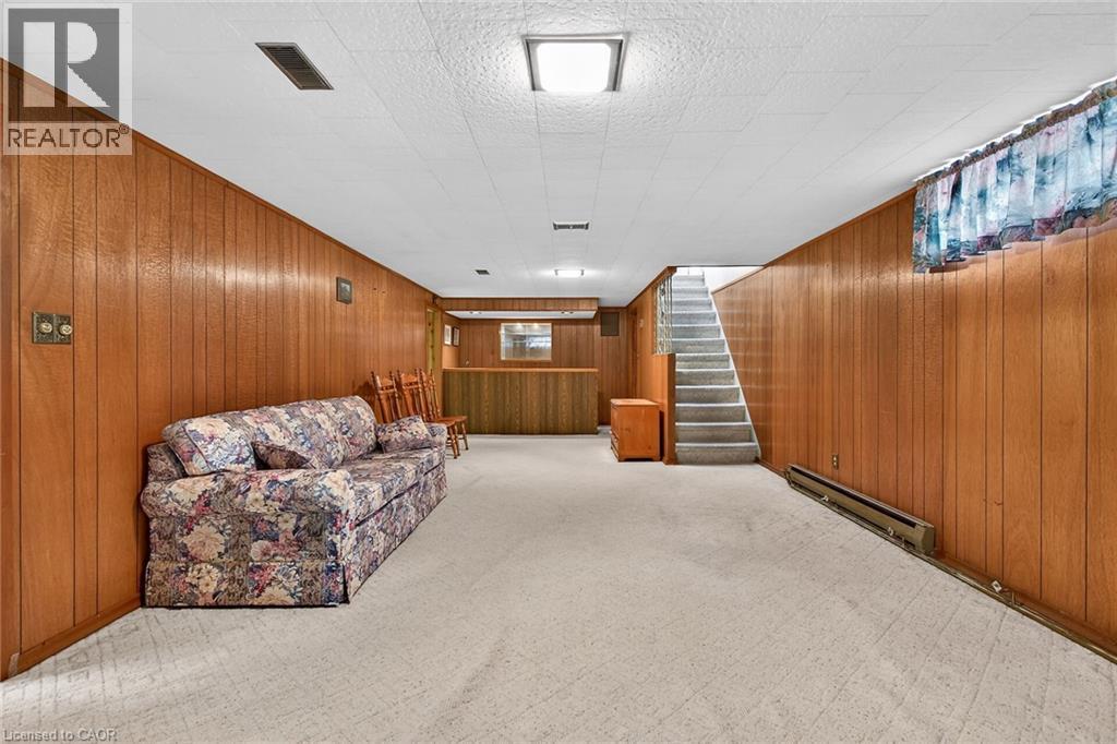 Living area featuring a baseboard radiator, wooden walls, and light carpet - 21 Bluebird Avenue, Hamilton, ON
