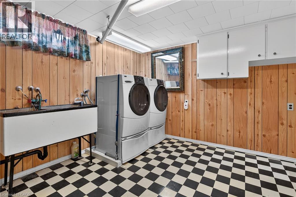 Laundry area featuring light flooring, wooden walls, and washing machine and clothes dryer - 21 Bluebird Avenue, Hamilton, ON