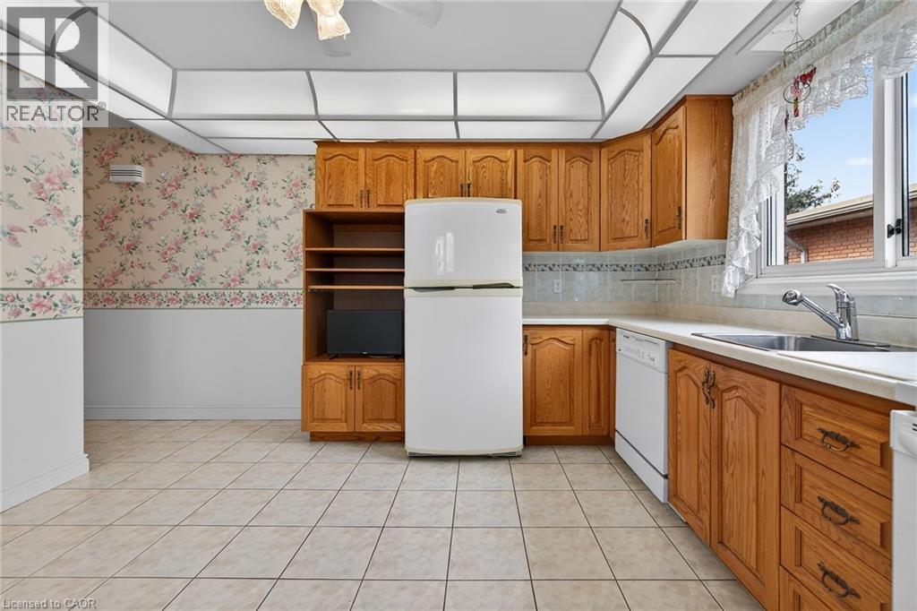 Kitchen with wood finish cabinetry, white appliances, wainscoting, light countertops, and wallpapered walls - 21 Bluebird Avenue, Hamilton, ON - Indoor Photo Showing Kitchen