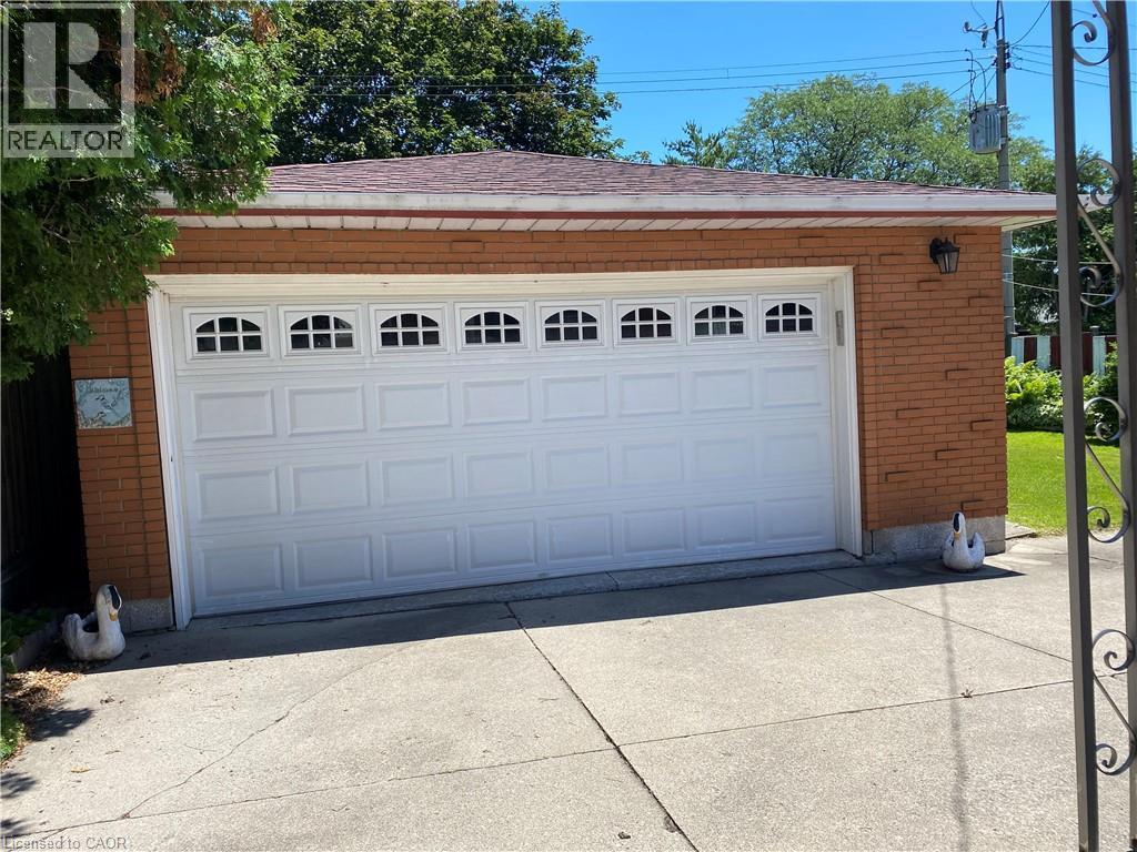 Attached two-car garage featuring a white panel door with arched window inserts, brick exterior, and a shingle roof - 21 Bluebird Avenue, Hamilton, ON