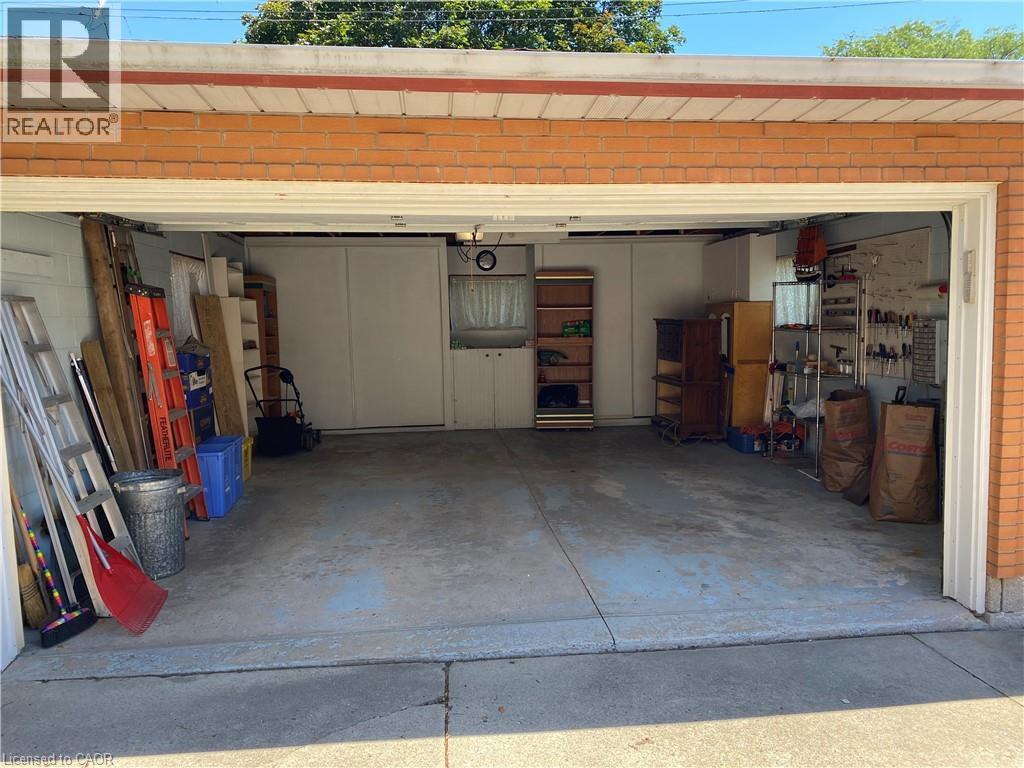 Attached two-car garage with a concrete floor, brick exterior, and built-in shelving and cabinetry for organized storage - 21 Bluebird Avenue, Hamilton, ON