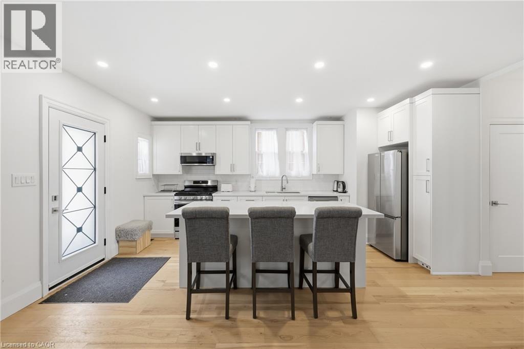 Kitchen with a breakfast bar, stainless steel appliances, white cabinets, a center island, and light wood finished floors - 129 Jackson Street W, Hamilton, ON - Indoor