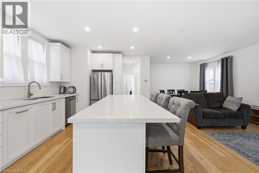 Kitchen featuring a breakfast bar, stainless steel appliances, a kitchen island, light wood-style floors, and white cabinetry - 129 Jackson Street W, Hamilton, ON - Indoor Photo Showing Kitchen With Upgraded Kitchen