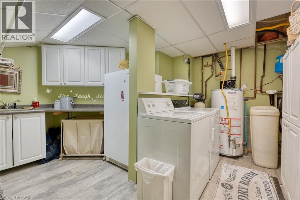 Laundry area featuring a drop ceiling, cabinet space, washer and clothes dryer, gas water heater, and light wood-style flooring - 15 Marquette Drive, Kitchener, ON - Indoor Photo Showing Laundry Room
