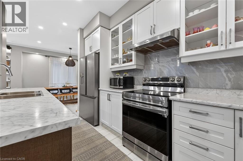 Kitchen with stainless steel appliances, glass insert cabinets, white cabinets, decorative backsplash, and decorative light fixtures - 7809 Hackberry Trail E, Niagara Falls, ON - Indoor Photo Showing Kitchen With Double Sink With Upgraded Kitchen