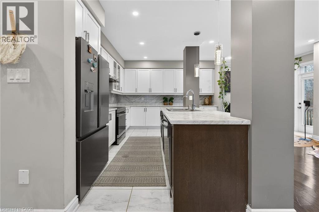 Two tone kitchen with light countertops, decorative light fixtures, stainless steel appliances, tasteful backsplash, and an island with sink - 7809 Hackberry Trail E, Niagara Falls, ON - Indoor Photo Showing Kitchen With Upgraded Kitchen