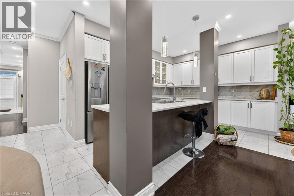 Kitchen with white cabinetry, stainless steel fridge with ice dispenser, light stone countertops, and decorative light fixtures - 7809 Hackberry Trail E, Niagara Falls, ON - Indoor