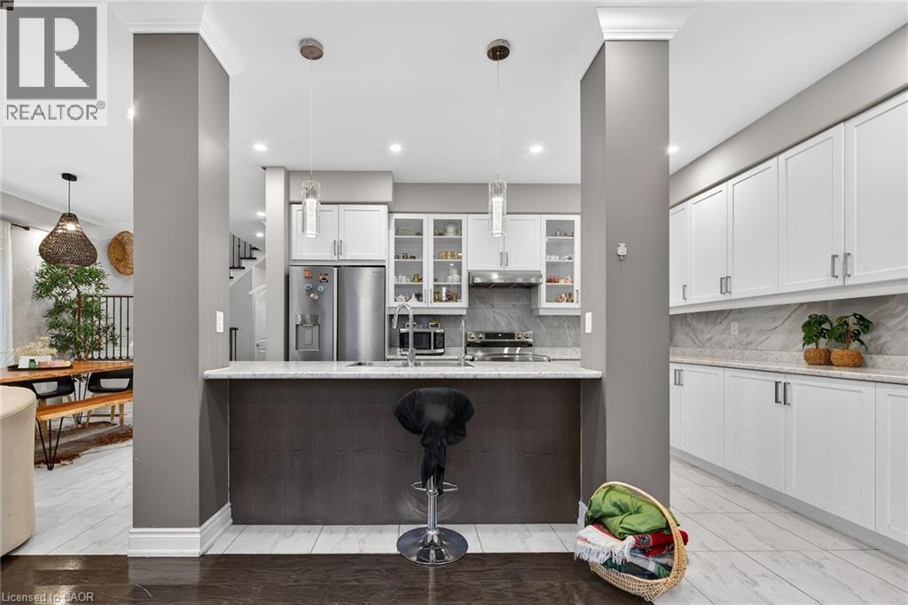 Kitchen with hanging light fixtures, white cabinetry, glass fronted cabinets, stainless steel appliances, and light stone counters - 7809 Hackberry Trail E, Niagara Falls, ON - Indoor Photo Showing Kitchen With Upgraded Kitchen