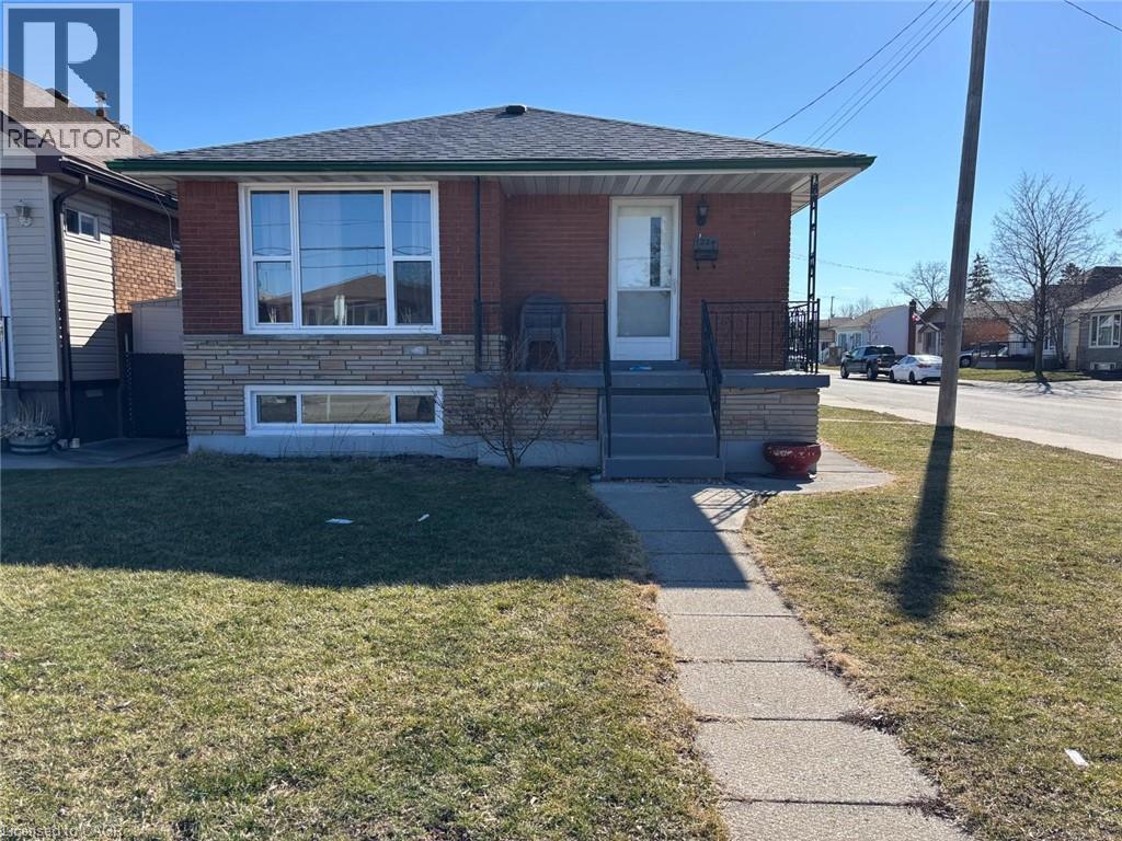 Bungalow featuring a front yard, covered porch, stone siding, brick siding, and roof with shingles - 1224 Dunsmure Road, Hamilton, ON - Outdoor