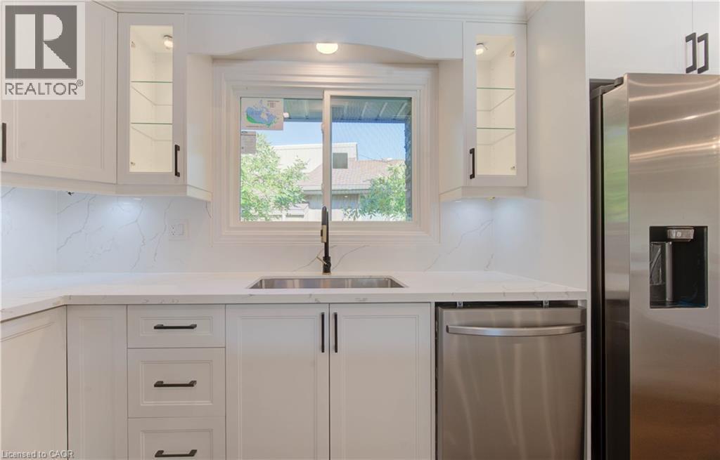 Kitchen with white cabinets, stainless steel appliances, glass insert cabinets, and light stone counters - 90 Culpepper Drive, Waterloo, ON - Indoor Photo Showing Kitchen