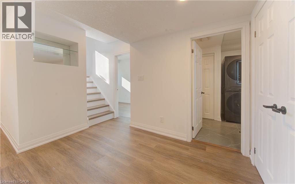 Spare room featuring light wood-style flooring, stacked washer and clothes dryer, and stairway - 90 Culpepper Drive, Waterloo, ON - Indoor Photo Showing Other Room
