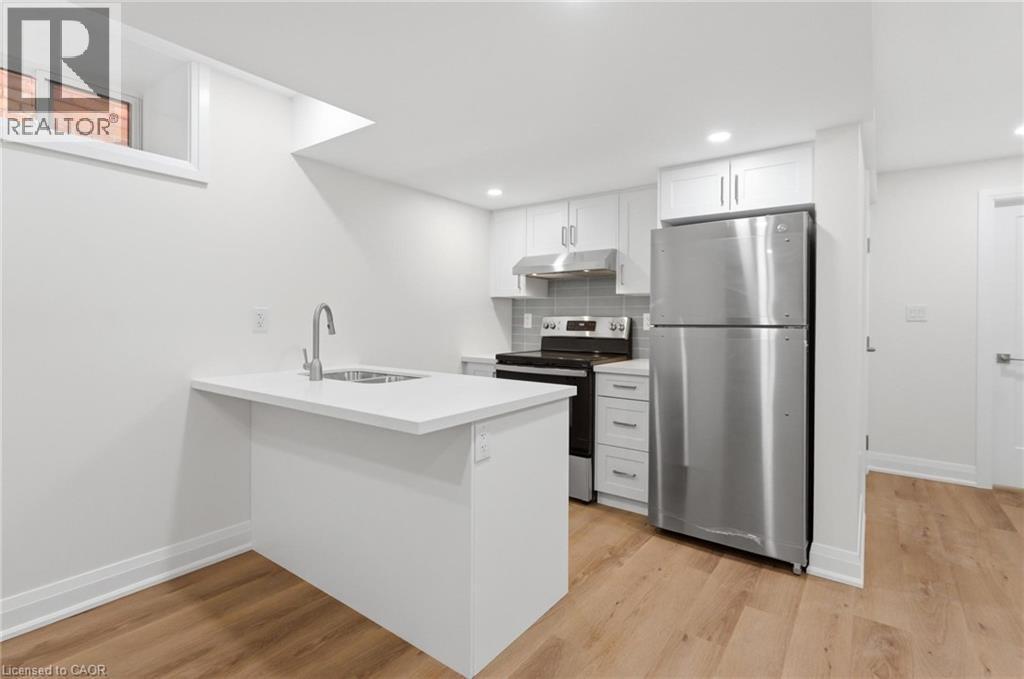 Kitchen featuring stainless steel appliances, white cabinetry, a peninsula, light wood-style flooring, and backsplash - 187 Oak Avenue Unit# Lower, Hamilton, ON - Indoor Photo Showing Kitchen