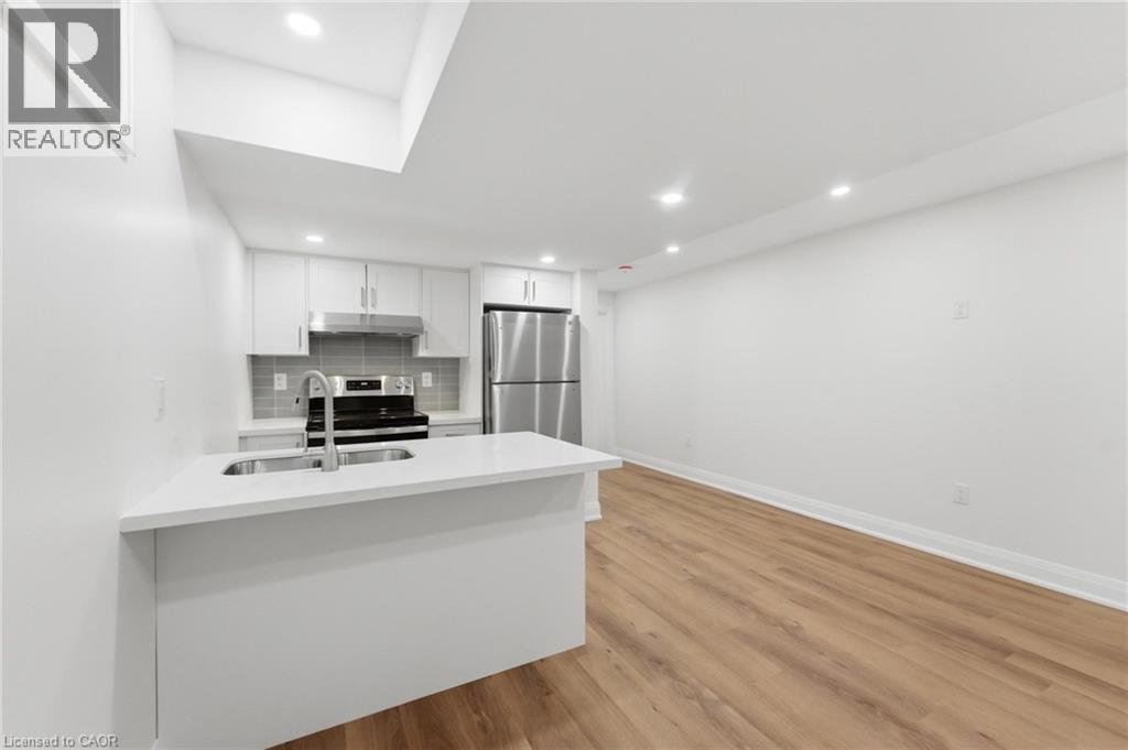 Kitchen featuring a peninsula, white cabinets, stainless steel appliances, light wood finished floors, and tasteful backsplash - 187 Oak Avenue Unit# Lower, Hamilton, ON - Indoor Photo Showing Kitchen With Double Sink