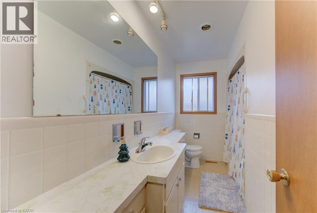 Full bath featuring vanity, tile walls, a shower with shower curtain, a wainscoted wall, and light tile patterned floors - 98 Shea Crescent, Kitchener, ON - Indoor Photo Showing Bathroom