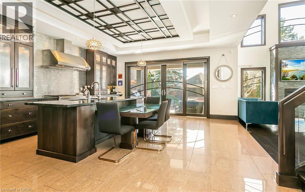 Kitchen featuring an island with sink, glass fronted cabinets, dark wood finish cabinets, a tray ceiling, and decorative backsplash - 24 Jacob Gingrich Drive, Kitchener, ON - Indoor