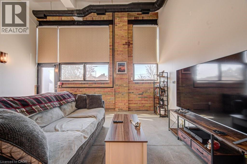 Living area featuring a high ceiling, brick wall, and carpet flooring - 85 Spruce Street Unit# 103, Cambridge, ON - Indoor