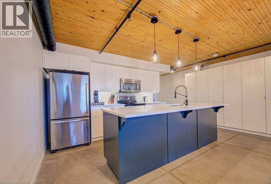 Kitchen with stainless steel appliances, wooden ceiling, decorative light fixtures, an island with sink, and a kitchen bar - 85 Spruce Street Unit# 103, Cambridge, ON - Indoor Photo Showing Kitchen With Stainless Steel Kitchen