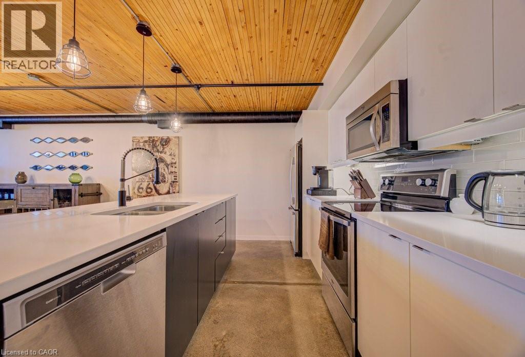 Dual tone kitchen with stainless steel appliances, finished concrete floors, pendant lighting, wooden ceiling, and backsplash - 85 Spruce Street Unit# 103, Cambridge, ON - Indoor Photo Showing Kitchen With Double Sink