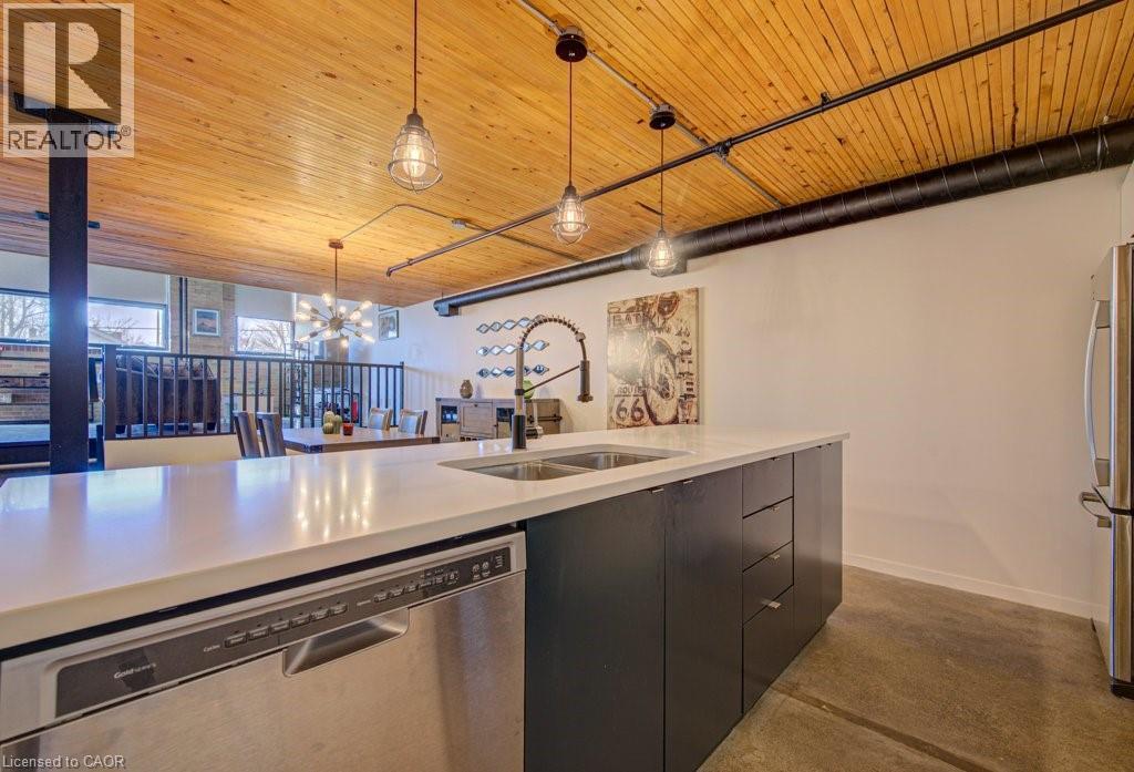Kitchen featuring stainless steel appliances, finished concrete floors, dark cabinets, wooden ceiling, and suspended lighting - 85 Spruce Street Unit# 103, Cambridge, ON - Indoor Photo Showing Kitchen With Double Sink