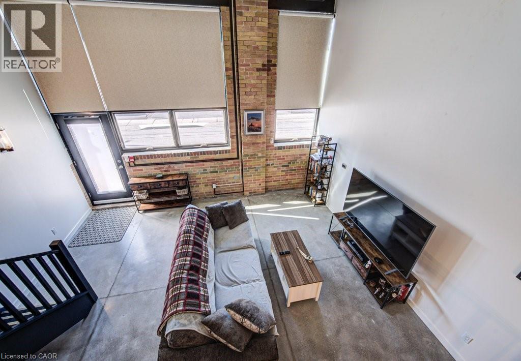 Living area featuring concrete floors, a high ceiling, plenty of natural light, and brick wall - 85 Spruce Street Unit# 103, Cambridge, ON - Indoor