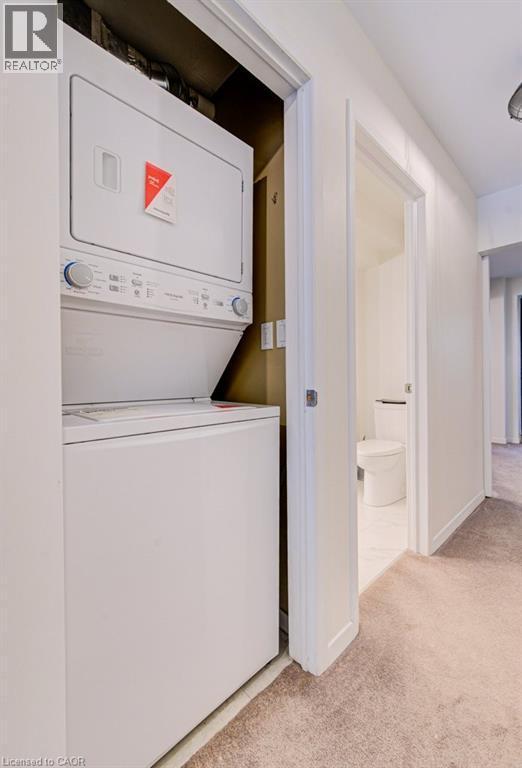 Laundry area with light colored carpet and stacked washer / dryer - 85 Spruce Street Unit# 103, Cambridge, ON - Indoor Photo Showing Laundry Room