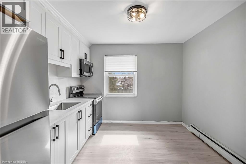 Kitchen featuring stainless steel appliances, white cabinets, baseboard heating, and light wood finished floors - 151 Siebert Avenue, Kitchener, ON - Indoor Photo Showing Kitchen