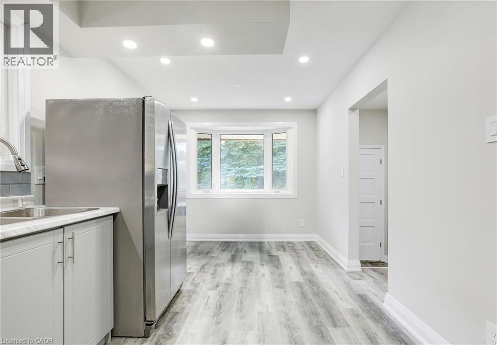 Kitchen with light countertops, stainless steel refrigerator with ice dispenser, light wood-style flooring, white cabinetry, and recessed lighting - 7 Cardill Crescent, Waterloo, ON - Indoor Photo Showing Kitchen With Double Sink
