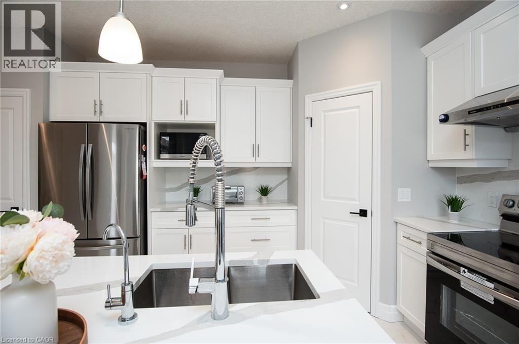 Kitchen featuring stainless steel appliances, white cabinetry, hanging light fixtures, light stone counters, and a textured ceiling - 346 Chokecherry Crescent, Waterloo, ON - Indoor Photo Showing Kitchen With Upgraded Kitchen
