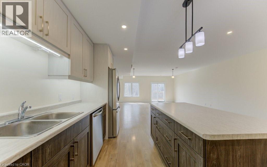 Kitchen featuring light countertops, light wood finished floors, a large island, stainless steel appliances, and hanging light fixtures - 113 Walter Street, Kitchener, ON - Indoor Photo Showing Kitchen With Double Sink