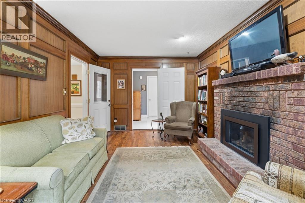 Living room with ornamental molding, wooden walls, wood finished floors, and a brick fireplace - 668 Tomahawk Crescent, Ancaster, ON - Indoor Photo Showing Living Room With Fireplace