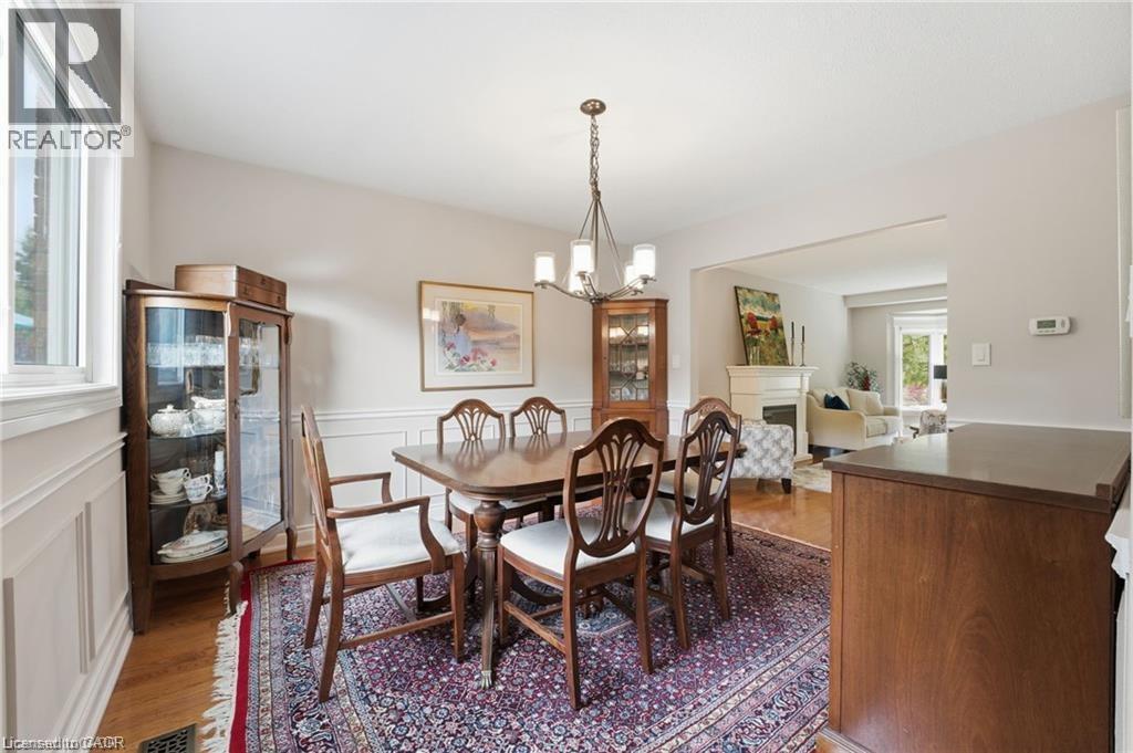 Dining room with a fireplace, light wood-style flooring, a decorative wall, a chandelier, and a wainscoted wall - 668 Tomahawk Crescent, Ancaster, ON - Indoor Photo Showing Dining Room